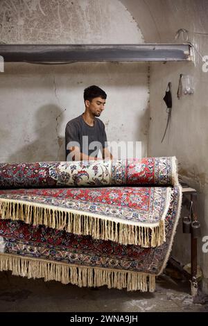 Ein Arbeiter rollt fertige Teppiche in einer kleinen Teppichherstellungswerkstatt. Yazd, Iran. Stockfoto