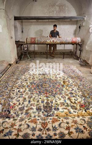 Ein Arbeiter rollt fertige Teppiche in einer kleinen Teppichherstellungswerkstatt. Yazd, Iran. Stockfoto