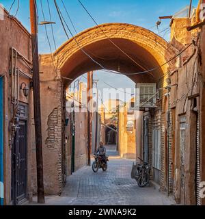 Ein Mann auf dem Motorrad fährt in einer engen Straße durch einen Bogengang im historischen Fahadan Viertel Yazd, Iran. Stockfoto