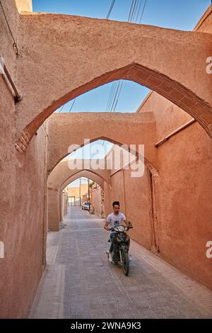 Ein Mann auf dem Motorrad fährt in einer engen Straße mit Bögen über dem historischen Fahadan Viertel Yazd, Iran. Stockfoto