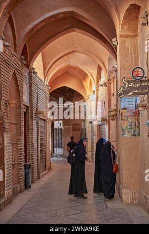 Drei einheimische Frauen in Chadors laufen in einer engen überdachten Straße in der Altstadt von Yazd, Iran. Stockfoto