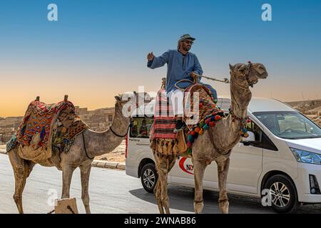 Gizeh Nekropolis, Ägypten - 26. April 2022: Lustiger spezifischer Verkehr mit Kamelen, Autos und Beduinen in der Nähe des Pyramidenkomplexes von Gizeh. Stockfoto