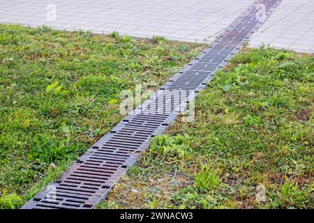 Langer Regenabfluss auf Gras und Gehsteig aus nächster Nähe Stockfoto