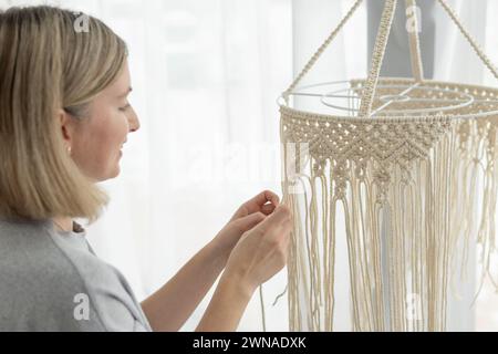 Eine schlanke, schöne Frau mittleren Alters strickt Produkte für den Innenraum mit Makramee-Technik Stockfoto