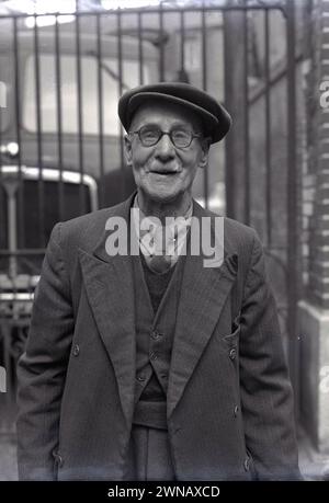 1950er Jahre, historisches Foto, das Bill Baker zeigt, einen langjährigen Mitarbeiter mit 60 Jahren treuer Arbeit, der an den Werkstoren seines ehemaligen Arbeitgebers Lucys, Oxford, England, Großbritannien, stand. Das Geschäft von W. Lucy & Co stammt aus dem Jahr 1812, als William Carter ein Eisenwarengeschäft an der Oxford High Street eröffnete. 1825 zog es in eine neue Messing- und Eisengießerei in Jericho, Oxford, die später als Eagle Works bekannt war. Stockfoto