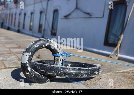 Dünnes Nylonseil, das an einen großen eisernen Festmacherring mit Schiff und Fenstern im Hintergrund gebunden ist Stockfoto