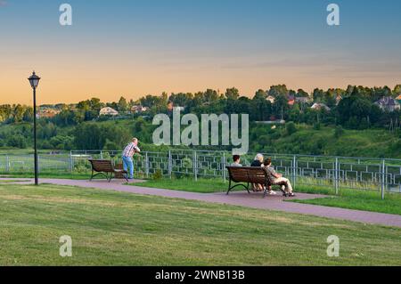 23. Juli 2022 Russland Tver Region Rzhev Stadt. Die Leute sitzen auf einer Bank am Ufer des Wolga-Flusses. Sie ruhen sich an einem sonnigen, warmen Abend aus. Lifestyle Stockfoto