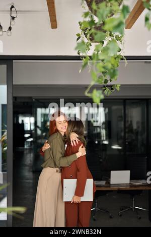 Zwei glückliche Geschäftsfrauen stehen bei der Arbeit im Büro, umarmt, vertikal. Stockfoto