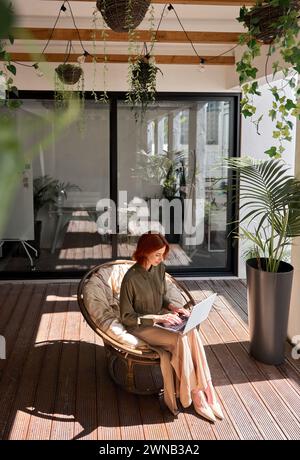 Geschäftsfrau mit Laptop, die in einem grünen Büro im Stuhl arbeitet. Draufsicht, vertikal Stockfoto
