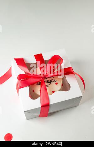 Weiße Box mit Kuchen, gebunden mit roter Schleife. Geschenkbox mit leckerem bento. Kuchenverpackung. Lieferung. Stockfoto