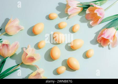 Gelbe Ostereier und Tulpenblüten auf grünem Hintergrund im Sonnenlicht. Osterkonzept. Draufsicht, flach. Stockfoto