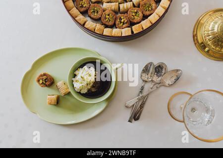 Trinken Sie Schokolade mit Sahne und Pistazien in passender grüner Tasse und Teller mit verschiedenen Baklava-Dessertdosen auf dem Tisch Stockfoto