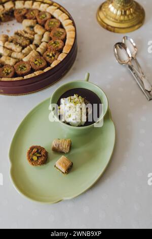 Trinken Sie Schokolade mit Sahne und Pistazien in passender grüner Tasse und Teller mit verschiedenen Baklava-Dessertdosen auf dem Tisch Stockfoto