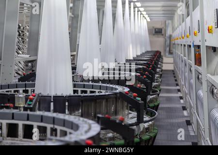 Innenraum eines Fabrikgeschäfts. Eine Reihe von Geräten zum Weben von Polypropylengewebe für Bausäcke in Perspektive. Verarbeitung von Rohstoffen. Stockfoto