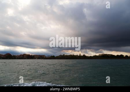 Venedig, Italien. Giudecca und Sacca San Biagio Inseln in der Lagune von Venedig mit dunkelblauem stürmischem Himmel im Hintergrund. Blick vom Wasserbus Stockfoto