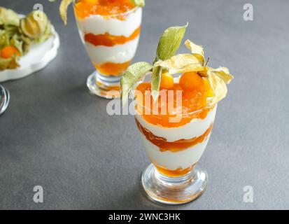 Mehrschichtiges Dessert mit Proteinjoghurt und Physalis-Früchten auf grauem Tisch Stockfoto