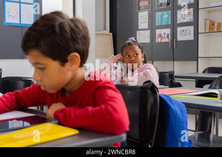 Ein birassischer Junge konzentriert sich auf seine Arbeit in einer Schulklasse, während ein birassisches Mädchen nachdenklich aussieht Stockfoto