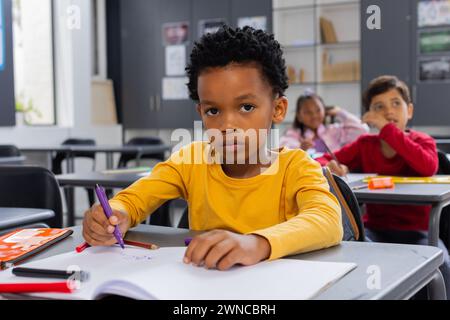 Ein afroamerikanischer Junge in einem gelben Hemd zeichnet in einer Schulklasse Stockfoto