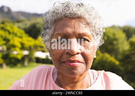 Ältere Frau mit lockigen grauen Haaren und einem sanften Lächeln steht draußen Stockfoto