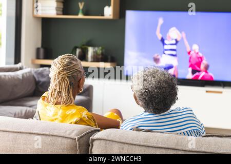Ältere afroamerikanische Frau und ältere birassische Frau schauen sich Rugby im Fernsehen zu Hause an Stockfoto
