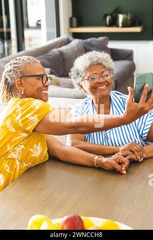 Ältere afroamerikanische Frau und ältere birassische Frau lächeln, während sie zu Hause ein Selfie machen Stockfoto