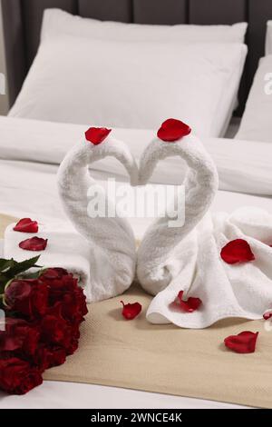 Flitterwochen. Schwäne aus Handtüchern und wunderschöne rote Rosen auf dem Bett Stockfoto