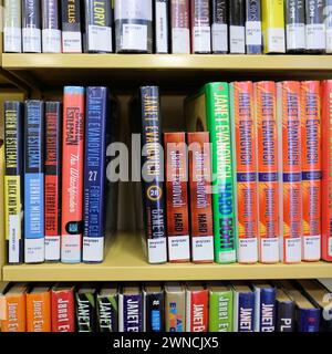 Bücherregal mit Mysterienromanen der amerikanischen Schriftstellerin Janet Evanovich; Stephanie Plum Series of Mysteries with Lücke left by missing book on Shelf. Stockfoto