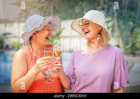 Seniorinnen trinken Wein in der Nähe des Pools im Urlaub im Freien Stockfoto