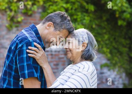 Ein hochrangiges birassisches Paar teilt einen zärtlichen Moment, in dem die Stirn mit einem liebevollen Lächeln berührt wird Stockfoto