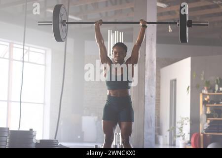 Starke birassische Frau hebt eine Langhantel in einem Fitnessstudio über sich Stockfoto