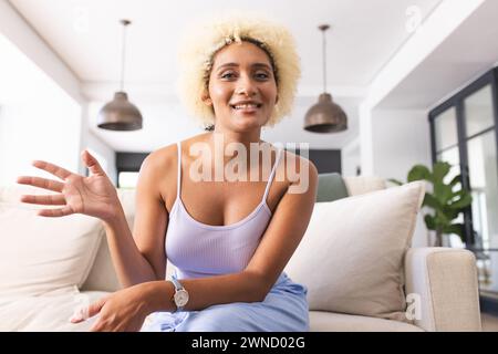 Junge Frau mit lockigen blonden Haaren lächelt beim Gesten im Videoanruf Stockfoto