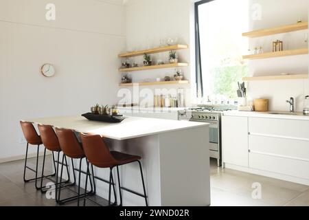 Die moderne Küche verfügt über eine zentrale Insel mit braunen Hockern und weißen Schränken und Kopierraum Stockfoto