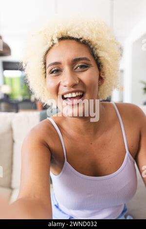 Eine junge Frau mit lockigen blonden Haaren lächelt bei einem Videoanruf in die Kamera Stockfoto