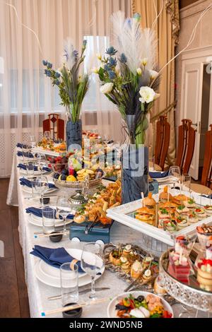 Ein dekadentes Buffet mit einer Auswahl an Snacks, Sandwiches, Obst und Süßigkeiten auf einem dekorierten Tisch. Feines porzellan, Gläser und Getränke erhältlich, Stockfoto