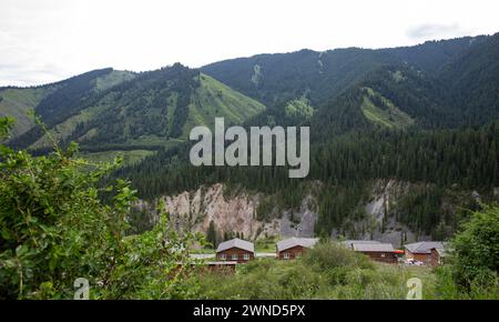 Traditionelles Kasachstans Jurtencamp im malerischen Bergtal in der Nähe des Flusses. Gemütliche Filz- und Holzjurten bieten lokale Gastfreundschaft inmitten von schneebedeckten Gipfeln. Stockfoto