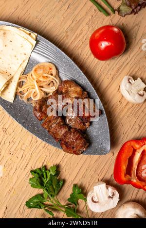 Saftiger Fleischkebab mit Gemüse und Kräutern auf einem Holztisch. Blick von oben. Stockfoto