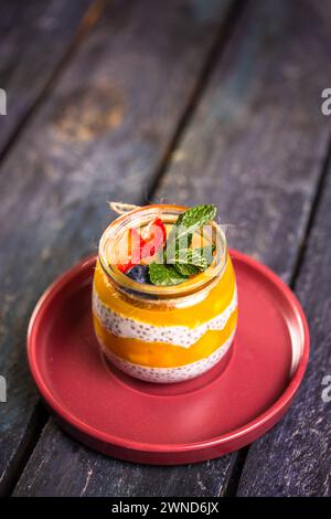 Chia Seed Pudding mit Mango und Beeren im Glasglas auf roter Platte Stockfoto