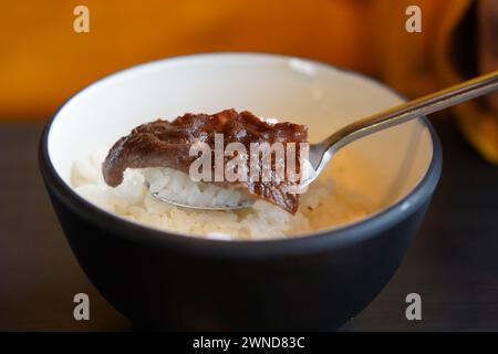 Reis und Rindfleisch in einer schwarzen Schüssel auf einem Holztisch. Stockfoto