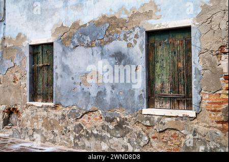 Ziegelsteine an einer alten Putzwand in Burano Italien mit zwei Holzfenstern. Stockfoto