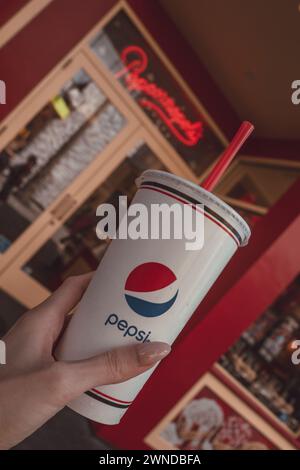 Weibliche Hand, die einen Plastikbecher mit Pepsi Cola und einem roten Strohhalm hält Stockfoto