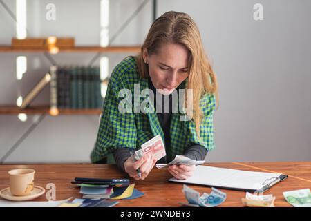 Eine junge hübsche Dame zählt nachdenklich und intensiv Geld für ein Designprojekt. Stockfoto