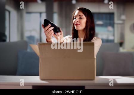 Lächelnde junge Frau sitzt auf einem Sofa Auspacken empfangene Paket Stockfoto