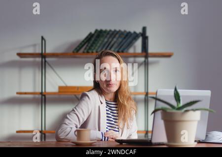 Eine junge, hübsche Geschäftsfrau freut sich mit einem diskreten Lächeln vor dem Hintergrund des Büros. Stockfoto
