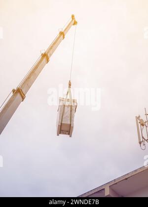 Industriekrane zum Betrieb und Anheben der elektrischen Box gegen Wolken und Himmel mit Telekommunikationsturm Stockfoto