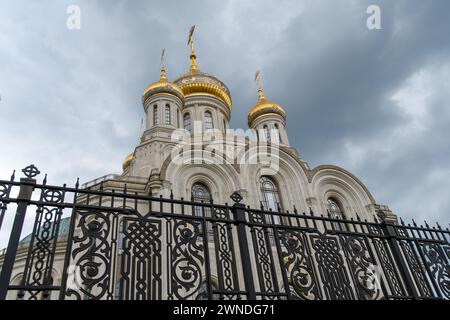 Die goldenen Kuppeln einer orthodoxen Kirche hinter einem geschmiedeten Zaun gegen den blauen Himmel. Stockfoto