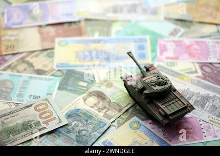 Kleiner grüner Tank auf vielen Banknoten verschiedener Währungen. Hintergrund der Kriegsfinanzierung oder Geld für die Verteidigung aus der Nähe Stockfoto