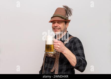 Älterer bärtiger Mann mit Hut will ein Glas Bier mit Schaum trinken, Bierfest in Österreich und Deutschland. Stockfoto