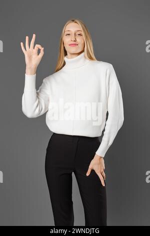 Die junge Frau in Hose und Pullover zeigt eine gute Geste Stockfoto