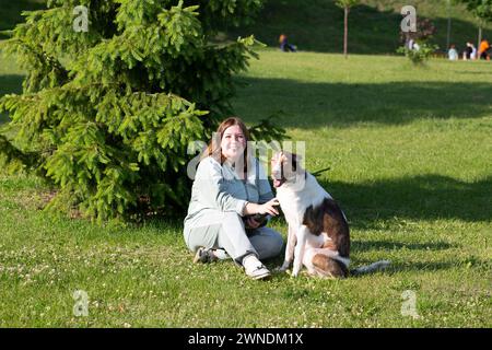 Eine Frau sitzt auf einer Wiese mit einem großen Hund im Sommer Russland Jaroslawl 10. August 2023 Stockfoto