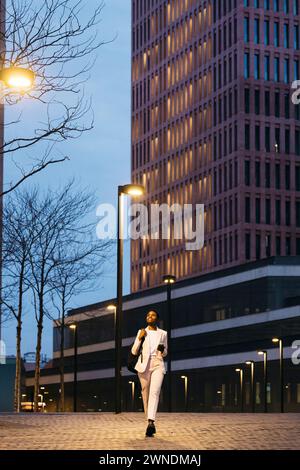 Junge, stilvolle Geschäftsfrau, die nachts nach der Arbeit auf einer Straße läuft. Lächelnde Geschäftsfrau, die nach der Arbeit nach Hause geht. Stockfoto
